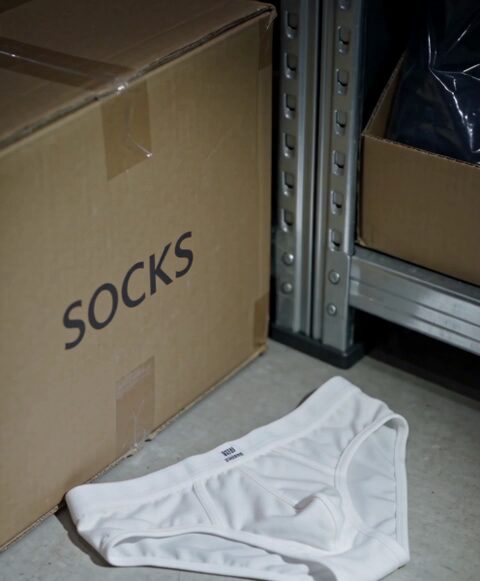 A carton marked SOCKS and a white garment wait by the stockroom shelving.