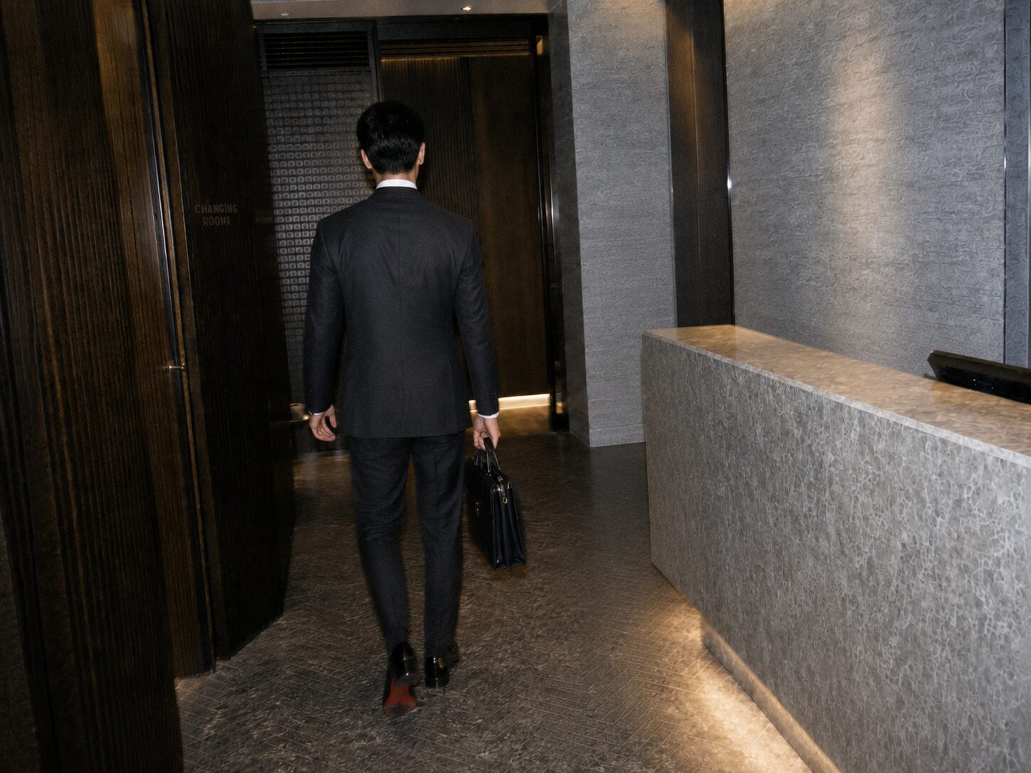 A suited man carrying a briefcase approaches the changing-room entrance beyond Shinrado reception.