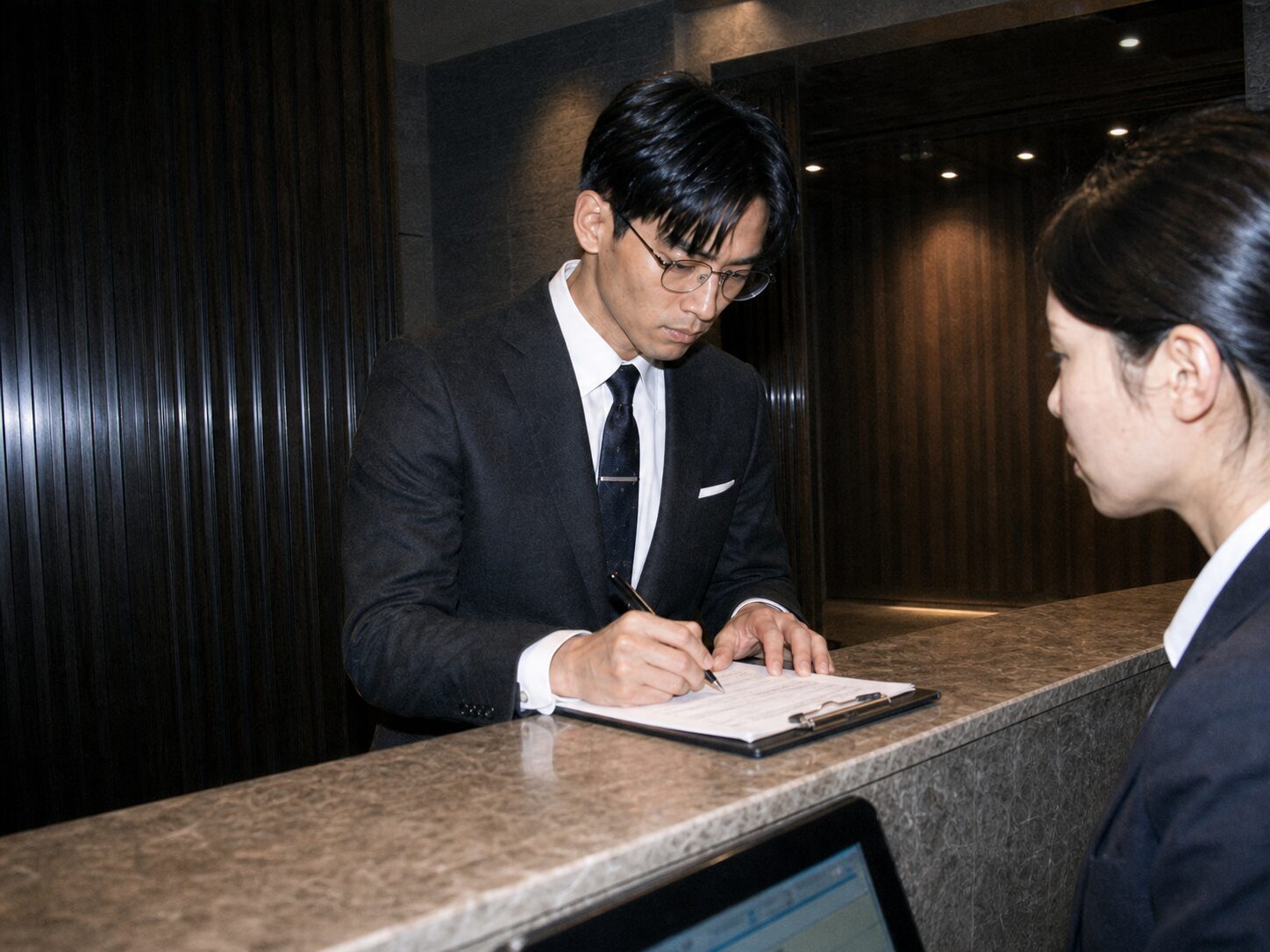A suited man completes a membership form at the Shinrado reception counter.